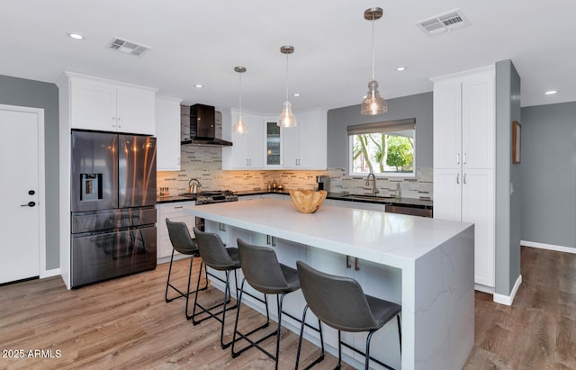 kitchen featuring wall chimney range hood, appliances with stainless steel finishes, white cabinetry, a kitchen island, and decorative light fixtures