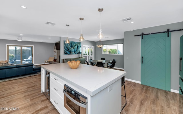 kitchen featuring a breakfast bar area, white cabinetry, a center island, hanging light fixtures, and a barn door