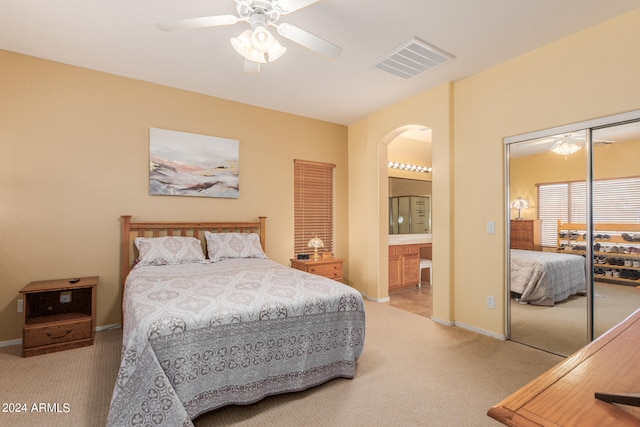 bedroom with a closet, ceiling fan, light colored carpet, and ensuite bathroom