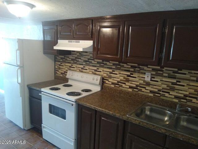 kitchen featuring dark brown cabinetry, sink, tasteful backsplash, light tile patterned floors, and white appliances