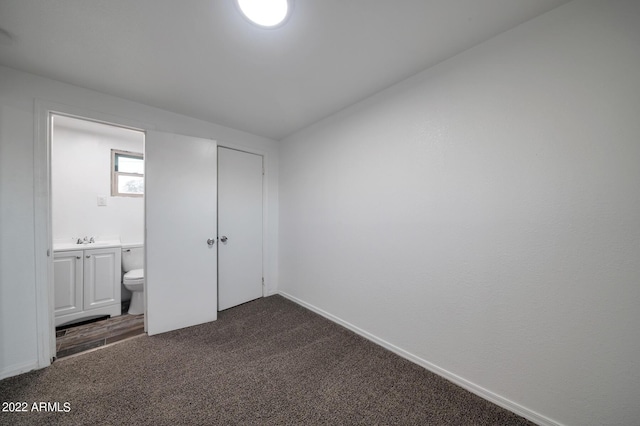 unfurnished bedroom with connected bathroom, sink, and dark carpet