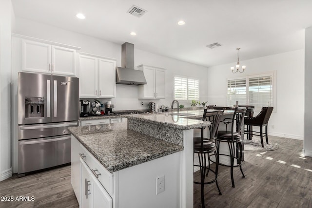 2052 E Scorpio Pl, Chandler, AZ 85249 - kitchen featuring stainless steel refrigerator with ice dispenser, wall chimney range hood, white cabinets, a breakfast bar area, and a chandelier