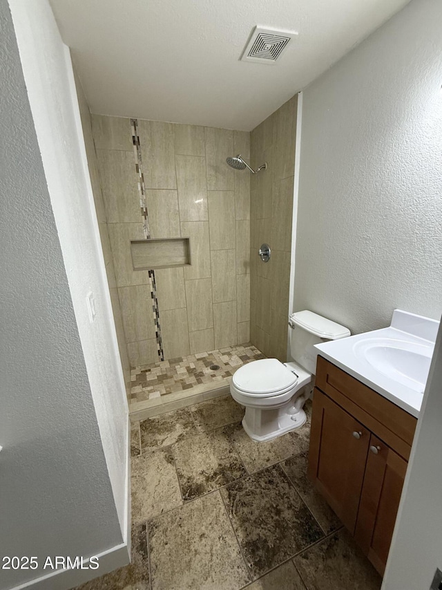 1841 N Wilbur Cir, Mesa, AZ 85201 - bathroom with vanity, a tile shower, toilet, stone finish flooring, and a textured wall