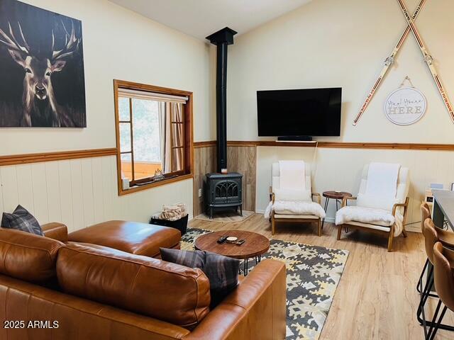 living room with a wainscoted wall, wood finished floors, a wood stove, and vaulted ceiling