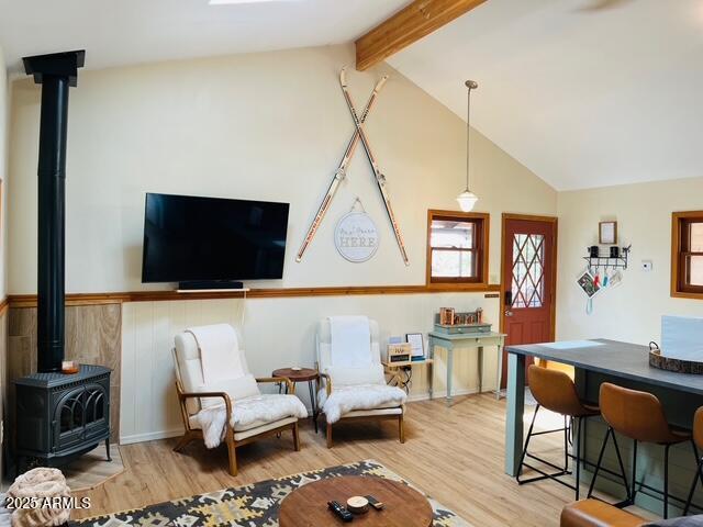 living area featuring lofted ceiling with beams, a wainscoted wall, light wood-style flooring, and a wood stove