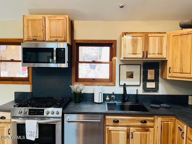 kitchen featuring dark countertops, light brown cabinets, appliances with stainless steel finishes, and a sink