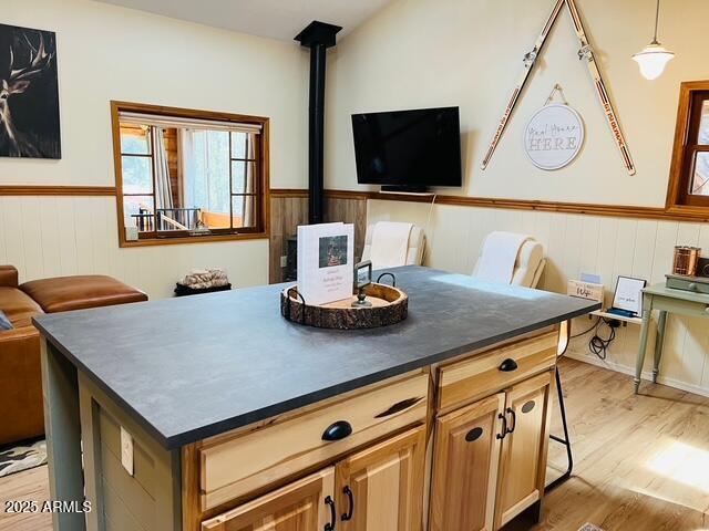 kitchen with a wood stove, light wood-style floors, wainscoting, dark countertops, and open floor plan