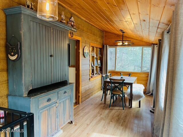 dining space with lofted ceiling, wooden walls, wood ceiling, and light wood finished floors