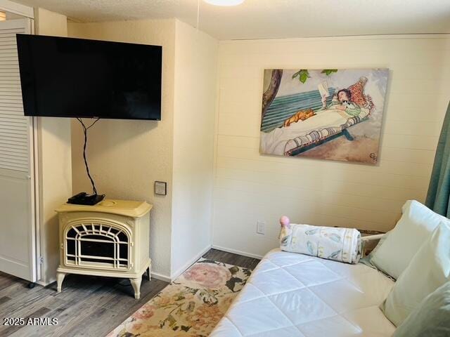 bedroom featuring a wood stove, baseboards, and wood finished floors