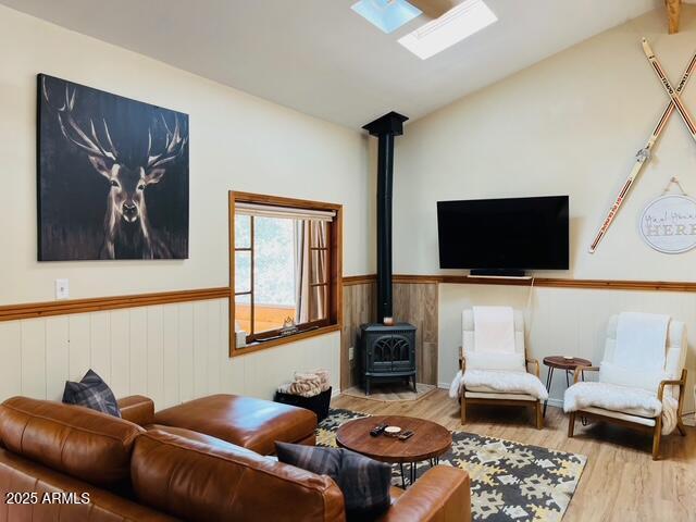 living room featuring wood finished floors, lofted ceiling with skylight, wainscoting, and a wood stove