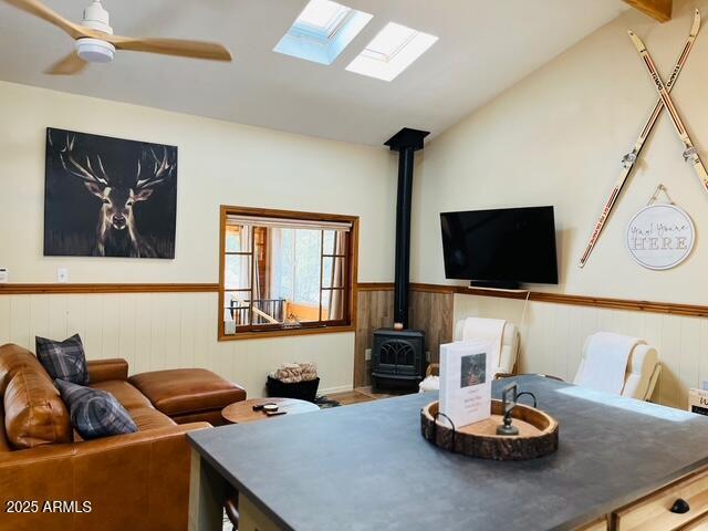 interior space with wainscoting, a ceiling fan, a wood stove, and lofted ceiling