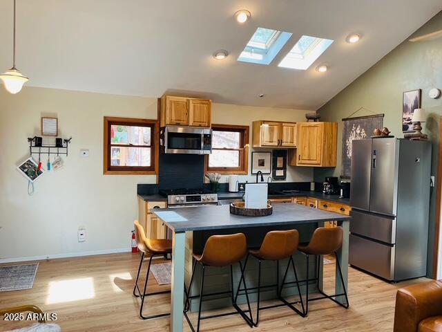 kitchen featuring light wood-type flooring, lofted ceiling with skylight, dark countertops, stainless steel appliances, and a breakfast bar area