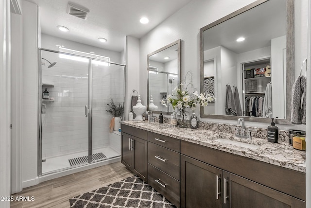 bathroom featuring visible vents, a shower stall, wood finished floors, and a sink