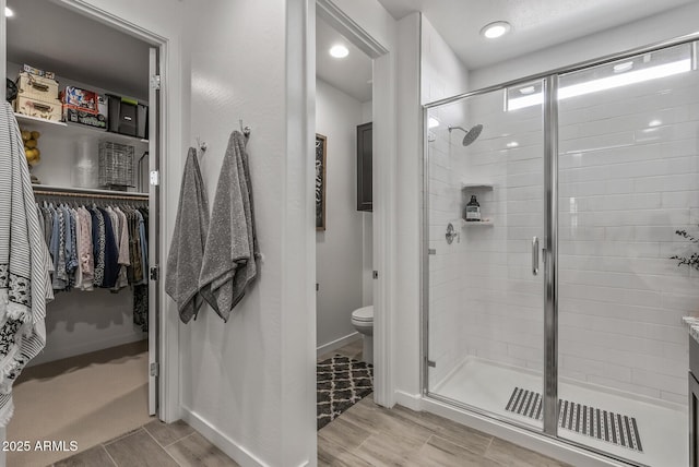 full bath featuring a shower stall, toilet, baseboards, and wood finished floors