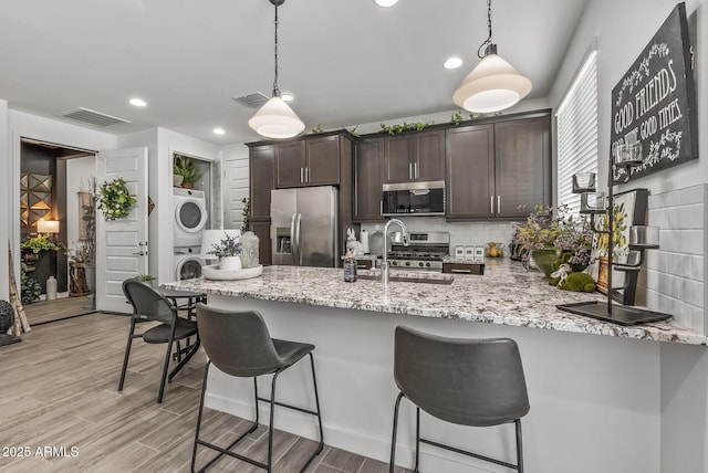 kitchen featuring stacked washer and clothes dryer, a sink, appliances with stainless steel finishes, decorative backsplash, and dark brown cabinets