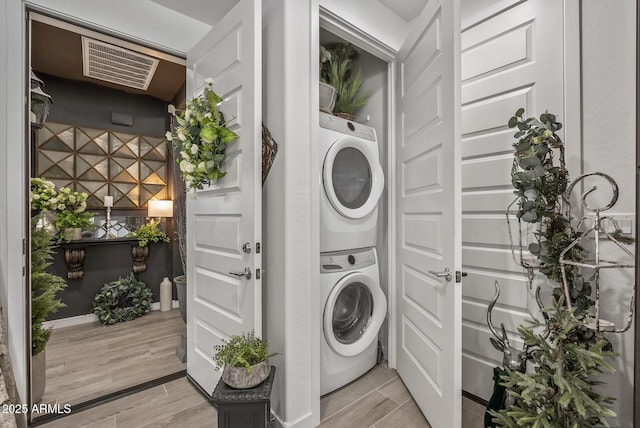 laundry area with laundry area, visible vents, stacked washer and clothes dryer, and wood finish floors