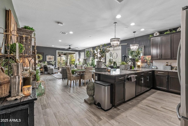 kitchen featuring dark brown cabinets, light stone counters, a peninsula, light wood-style floors, and stainless steel appliances