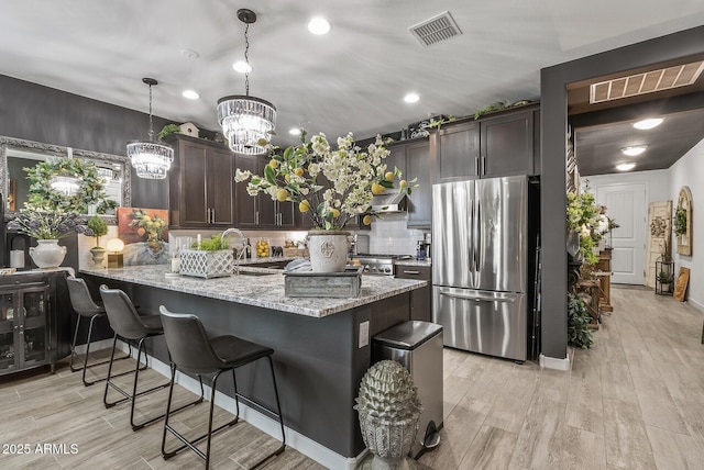 kitchen featuring light stone counters, visible vents, dark brown cabinetry, and freestanding refrigerator