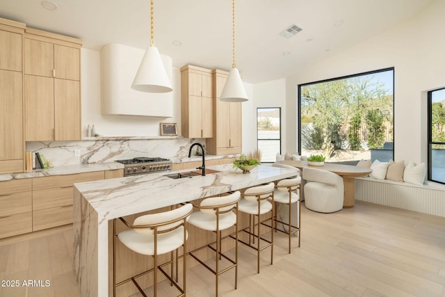 kitchen with a center island with sink, decorative backsplash, sink, and light brown cabinetry