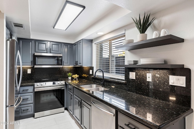 kitchen featuring gray cabinetry, dark stone counters, sink, tasteful backsplash, and stainless steel appliances