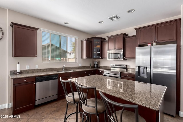 kitchen with stainless steel appliances, a sink, visible vents, dark brown cabinets, and glass insert cabinets