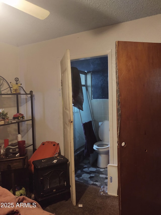 bathroom featuring a wood stove, a textured ceiling, and toilet