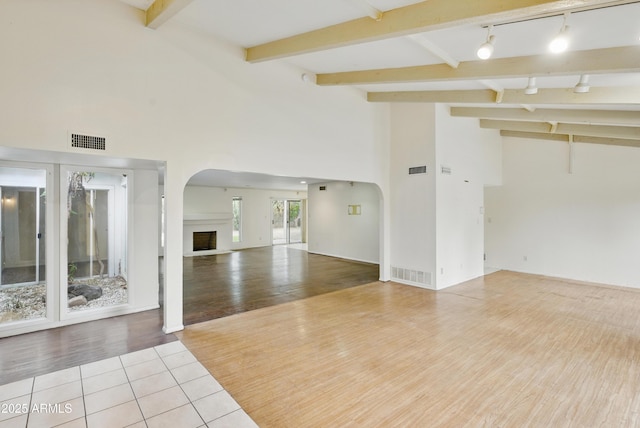 8411 E Via De Jardin, Scottsdale, AZ 85258 - unfurnished living room with arched walkways, track lighting, beam ceiling, wood finished floors, and a fireplace with raised hearth