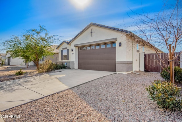 view of front of home with concrete driveway, a tiled roof, an attached garage, fence, and stucco siding