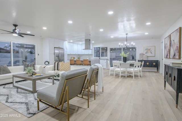 living room with sink, ceiling fan with notable chandelier, and light wood-type flooring