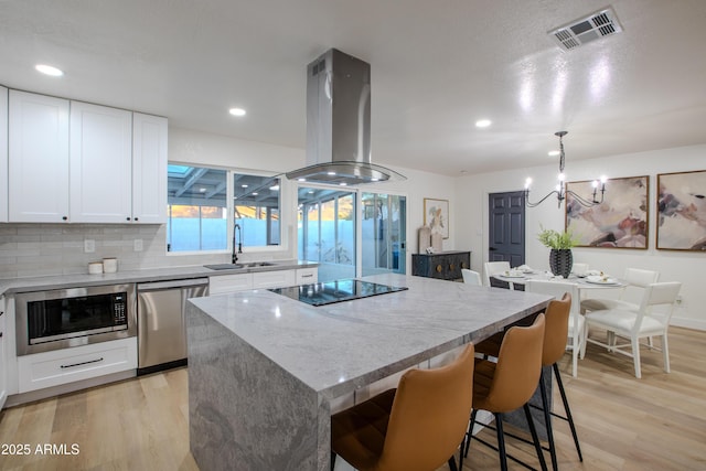 kitchen with sink, island range hood, a kitchen island, stainless steel appliances, and white cabinets