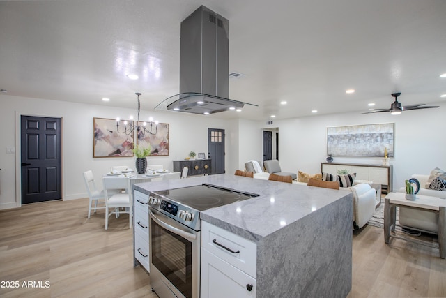 kitchen featuring pendant lighting, stainless steel electric range, island range hood, light stone countertops, and white cabinets