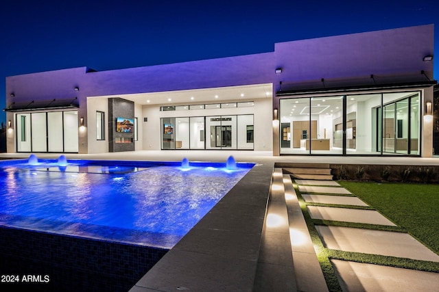 pool at night featuring pool water feature