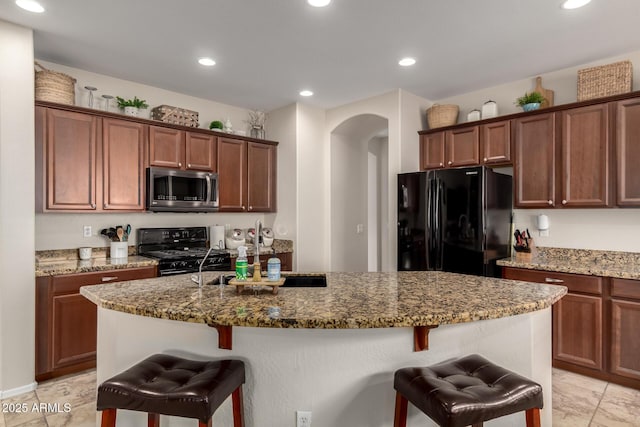 kitchen with a kitchen bar, black appliances, dark stone countertops, recessed lighting, and arched walkways