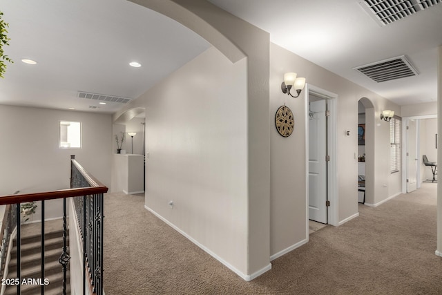 corridor featuring light carpet, visible vents, recessed lighting, and arched walkways