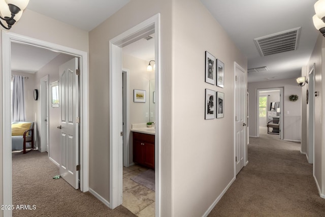 hallway with visible vents, baseboards, and light colored carpet