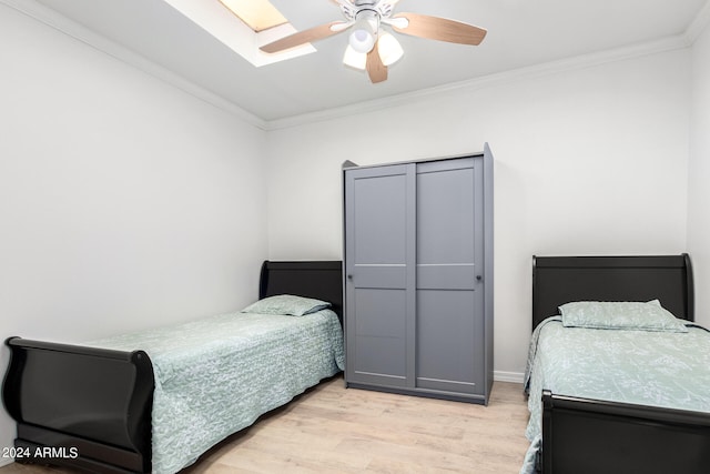 bedroom featuring a skylight, ceiling fan, ornamental molding, and light wood-type flooring