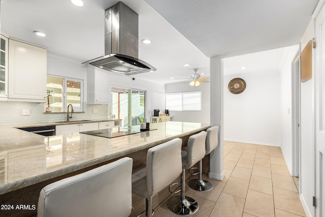 kitchen featuring light stone countertops, sink, range hood, a kitchen bar, and black electric cooktop