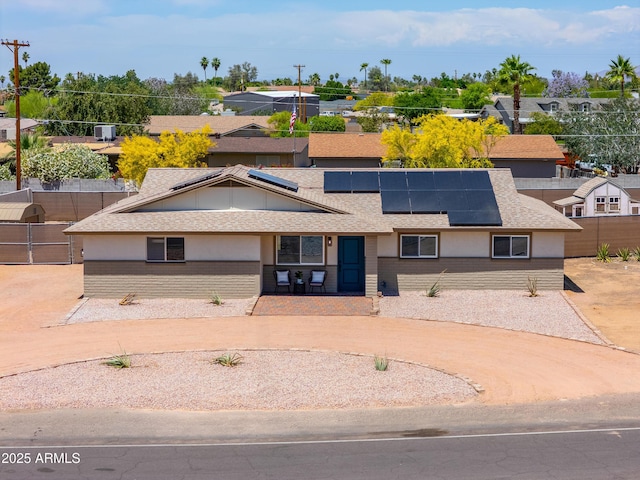 view of front of house featuring fence, a shingled roof, roof mounted solar panels, and a residential view