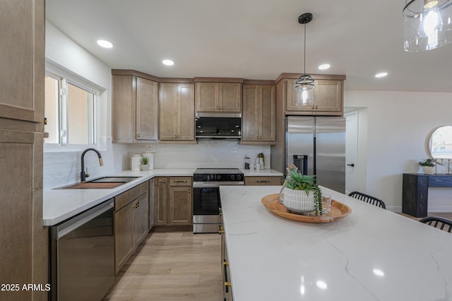 kitchen with decorative backsplash, appliances with stainless steel finishes, a sink, light stone counters, and light wood-style floors