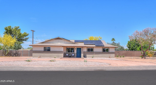 single story home with stucco siding, roof mounted solar panels, fence, and brick siding