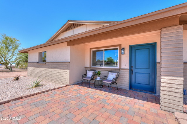 property entrance featuring stucco siding, a patio area, and brick siding