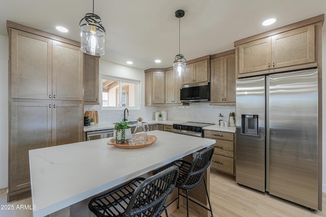 kitchen featuring decorative backsplash, a kitchen island, light wood-style floors, light stone counters, and appliances with stainless steel finishes
