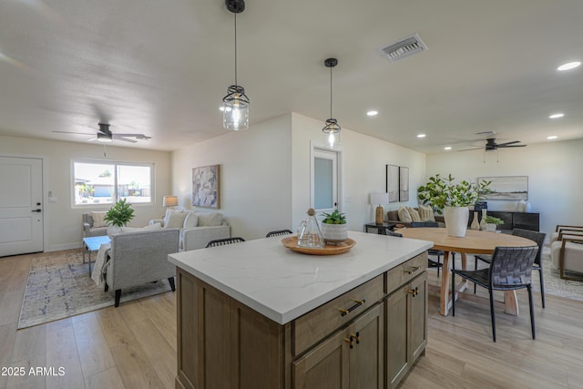 kitchen with open floor plan, visible vents, ceiling fan, and a center island