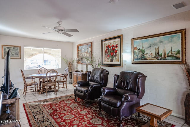 living area with ceiling fan, light tile patterned floors, and brick wall