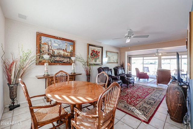 tiled dining room featuring ceiling fan and brick wall