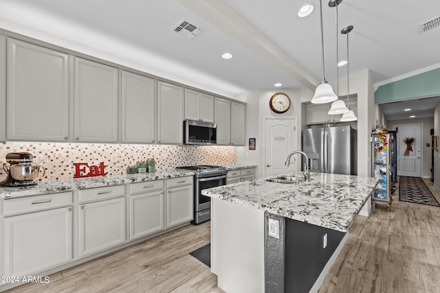 kitchen with light hardwood / wood-style floors, decorative light fixtures, sink, stainless steel appliances, and an island with sink