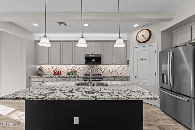 kitchen featuring stainless steel appliances, decorative light fixtures, a kitchen island with sink, and light wood-type flooring