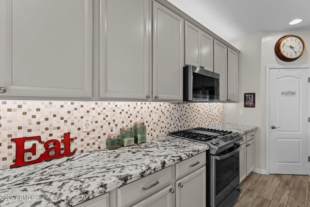 kitchen with light wood-type flooring, tasteful backsplash, gray cabinetry, stainless steel appliances, and light stone countertops