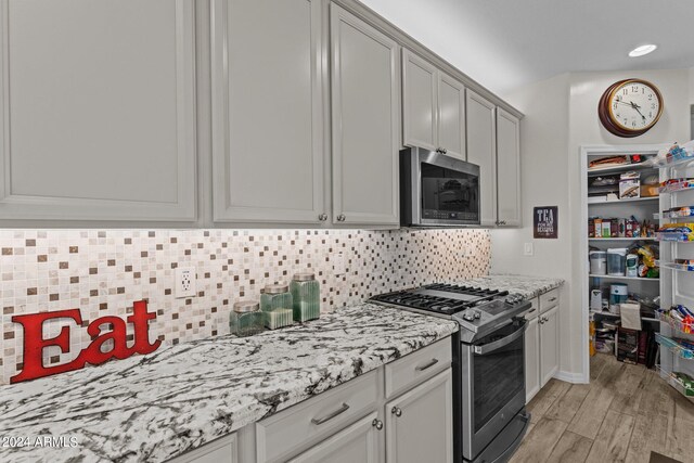 kitchen featuring light stone countertops, tasteful backsplash, gray cabinetry, light hardwood / wood-style floors, and appliances with stainless steel finishes