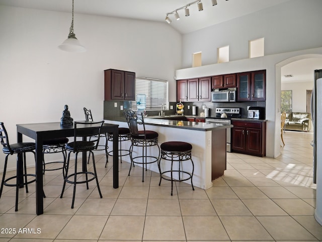 kitchen with dark countertops, stainless steel appliances, arched walkways, a breakfast bar area, and light tile patterned floors